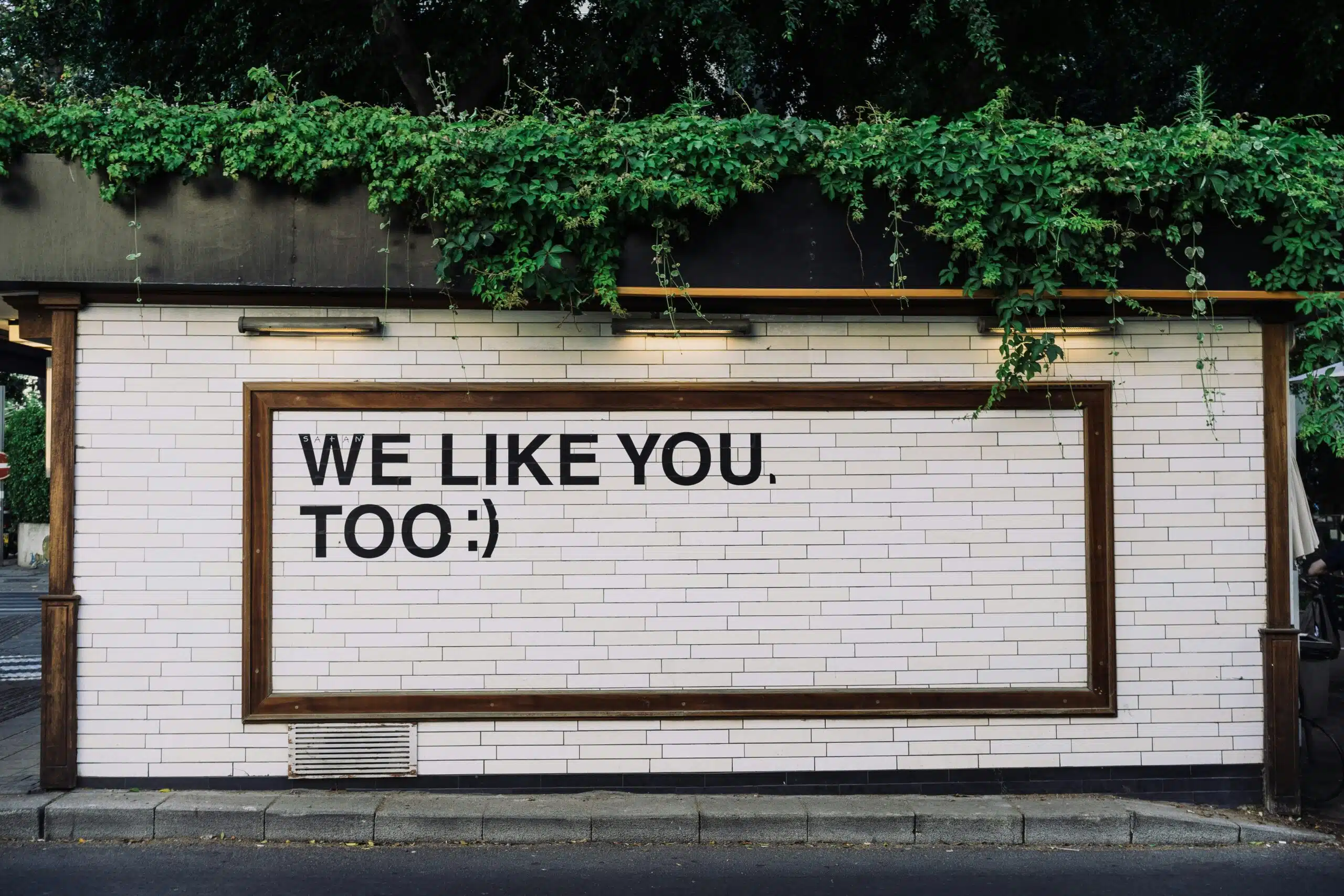 Photo of a wall mounted billboard, words are We Like You Too :-)